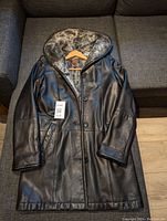 Front view of black leather ladies coat on hanger showing button-down front and fur-lined collar and cuffs.