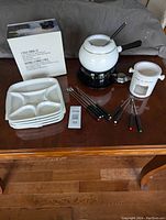 Photo showing all the items of the two fondue sets, including the fondue pots, plates, and forks arranged on a table.