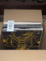 Box containing a stack of approximately 20 vinyl LP records with various cover designs, viewed from above and angled.