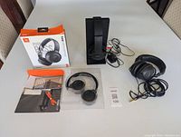 Three pairs of headphones laid out on table including Sony wireless charging set, Sony wired headphones, and JBL headphones in box with accessories.