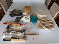 Full view of kitchen items including panini press, cookware, utensils, measuring cups, and wooden cutlery block arranged on table