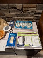 Photo shows packaged white rocker and toggle switches, 3 LED puck lights in a blister pack, and a white LED remote control puck light with remote.