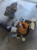 Photo showing the large net or rope bundle, metal tool box, come-along winch, joist hangers, and orange and blue Busy Bee Tools bag filled with hardware items.