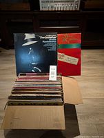 Box containing over 50 vinyl LP records including 'The Godfather' soundtrack and a Christmas themed album in front.