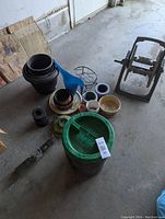 Overview photo showing concrete mixer, flower pots, watering jug, hose reel, and hanging glass hummingbird feeder among garden items on floor.