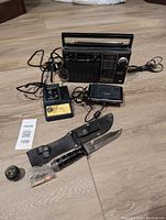 Photo of the complete lot showing all items including the radio, soldering station with iron and stand, GPS, and hunting knife with sheath and small accessories.