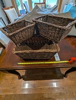 Three wicker baskets stacked together on a table with a measuring tape showing size.