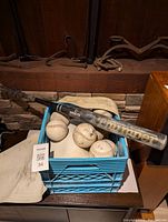 Blue plastic milk crate containing three softballs and a Worth Marathon metal softball bat resting on the crate with visible wear and tear on the bat and balls.