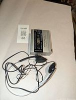 Top-down photo of the silver Realistic SCP 12 auto-reverse cassette player with attached foam-padded earphones and cable spread out.