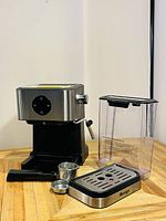 Espresso machine assembled with water tank, drip tray, portafilter, and accessories on wooden surface against white background