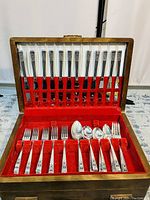 Front view of antique Community silver plated flatware set arranged in wooden box with red velvet lining, showing knives in upper section and forks/spoons below.