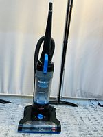 Full view of Bissell PowerForce upright vacuum cleaner showing black and blue color scheme with clear dust bin and attached hose.