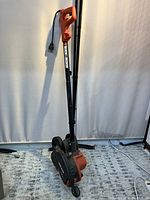 Front angled view of the Black & Decker LE750 Edge Hog 2-in-1 electric landscape edger showing the handle with power switch, electric cord, dual wheels around the blade area, and the Black & Decker label on the black handle tube.