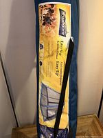 Blue carrying bag for Broadstone Easy Up Screen House with visible product label and shoulder strap, placed on wooden table.