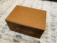 Brown carrying case closed, showing top with minor wear and textured surface.