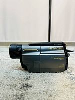 Side view of Hitachi VM camera showing model details, zoom specifications and branding.