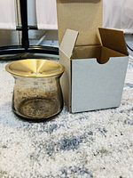 Photo showing the smaller, rounded glass vase next to its open cardboard box, on a light carpet.