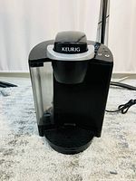 Front and left side view of black Keurig K-Classic coffee maker showing water reservoir, drip tray, and brewer opening