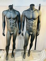 Two black male mannequins side by side on square bases in indoor setting.