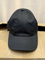 Front view of a black baseball cap showing 'less shiddy' embroidered text.
