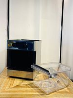 Front angle of the Pico Brewing Model S beer maker with clear plastic fermentation tank placed beside it on wooden surface.