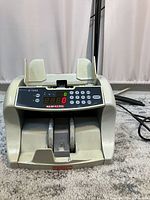 Front angled view of SEMACON S-1200 currency counter showing digital display, keypad, and dual note compartments with adjustable guides.