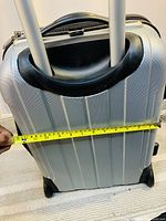 Photo showing the silver hard shell suitcase with a tape measure across it indicating approximately 13 inches width.