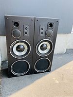 Both VIVID Thunder Series TX-440 loudspeakers shown side-by-side outdoors, visible drivers and controls, one speaker has fabric damage on lower grille.