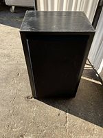 Front view of a wooden speaker with black grille, showing scratches on the top surface and signs of use