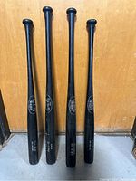 Four black Louisville Slugger baseball bats with NY Mets branding placed standing up against a wooden door.