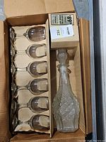 Boxed set with a crystal decanter and six matching wine glasses with packaging and original price tag visible.