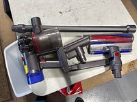 Dyson vacuum components including main handheld unit, extension wand, motorized brush head, and small attachments on a white table.