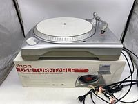 Silver Ion USB Turntable sitting on original box with power cord in front.