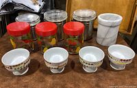 Glass and metal kitchen canisters, red-lid fruit decorated canisters, white marble wine chiller visible on wood surface