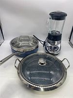 Photo showing both the Ninja strainer cooking pan with glass lid and the Cuisinart blender with glass jar and control buttons.