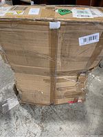 Large damaged cardboard box containing the treadmill, showing wear and tear from shipping and handling.