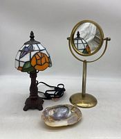 Stained glass lamp, brass vanity mirror, and shell dish together from the front