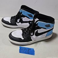 Side view of Nike Air Jordan 1 sneakers showing black, white, and light blue color pattern and Air Jordan wings logo on ankle.