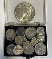 View of 1925 Peace Silver Dollar and multiple smaller silver coins in a small plastic case.
