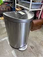 Metal trash can with brushed stainless steel finish, closed lid and foot pedal visible.