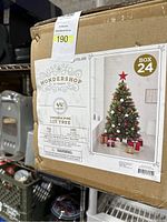 Box label showing brand, model, and specifications of the Christmas tree including 244 tips, 150 LEDs, 4.5 feet height, and image of the tree with star topper and gifts.