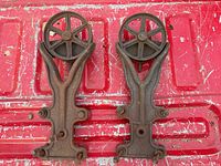 Pair of antique barn door rollers with visible rust, front view on red surface.