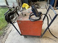 Side view of orange metal arc welder unit on wheeled frame with cables and torch wrapped on one side.