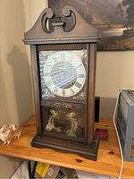 Full front view of vintage Carillon 31 day mantle clock showing wood case, glass door with clock face and pendulum.