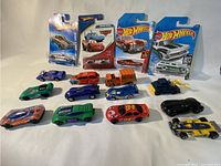 Photo of 16 assorted Hot Wheels diecast cars, including loose and packaged cars on a flat surface.