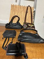 Five purses and small bags arranged on wooden floor showing different styles and materials.