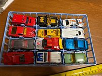 Top-down view of 12 toy cars in a blue plastic container showing detailed colors and vehicle types.