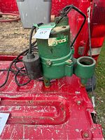 Side view of used green Myers sewage pump with power cords and float switch placed on red surface.