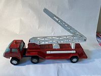Side view of the red pressed tin fire truck with lifted extendable silver ladder and black plastic wheels.