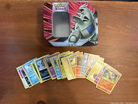Photo of Pokémon metal tin with Aggron design and Pokémon cards spread in front of it showing assortment and quantity.